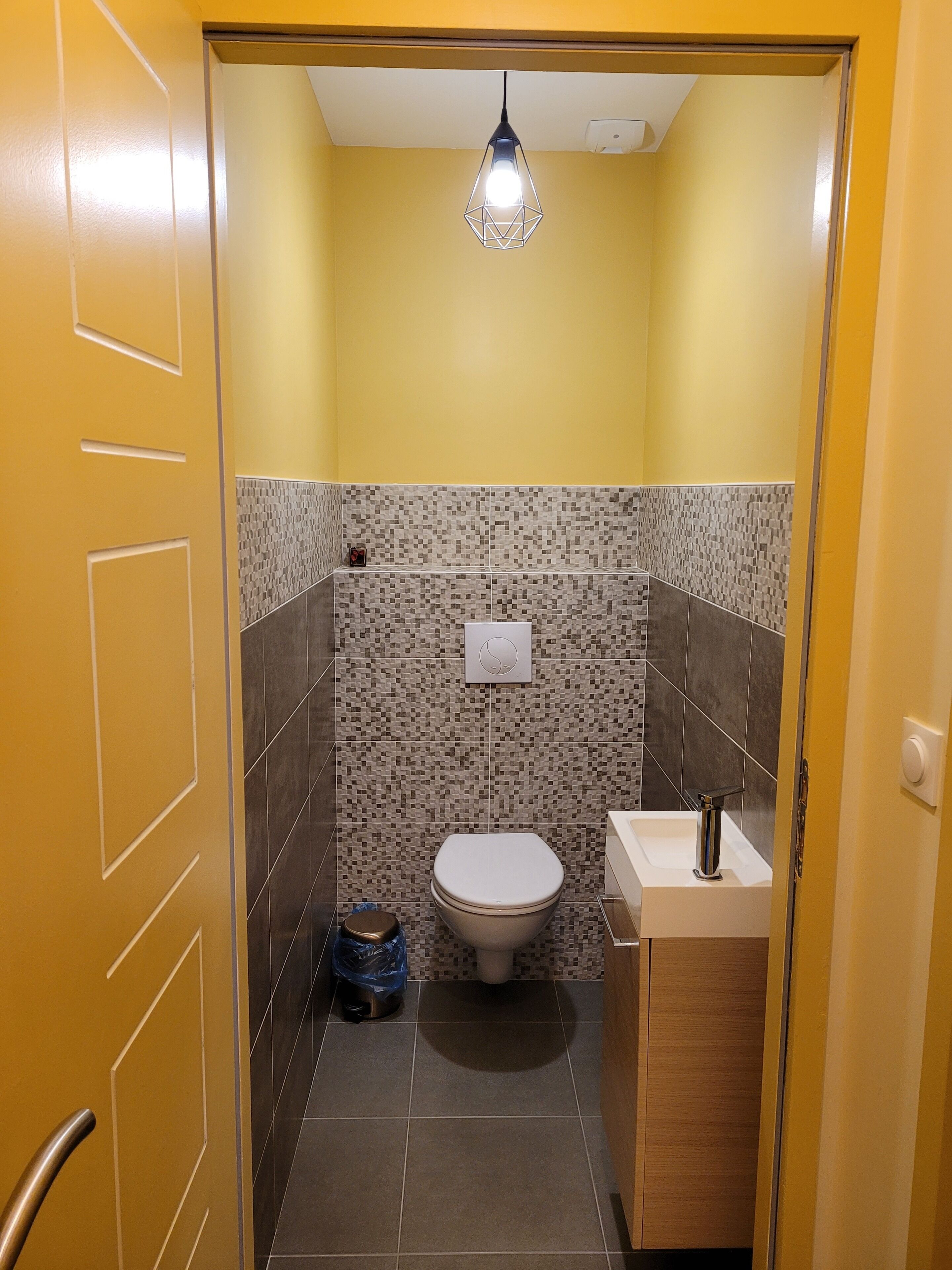 Een kleine badkamer met toilet, wastafel en een hangende lamp.