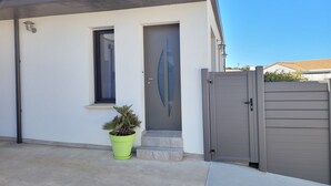 Una casa moderna con una puerta gris, un ventanal pequeño y una planta en maceta en la entrada.