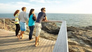 Un grupo de personas de pie en una terraza de madera con vista al mar.