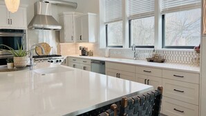 Une cuisine moderne avec des meubles blancs, un grand îlot central, des appareils en acier inoxydable et des luminaires suspendus.