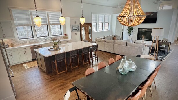 Une cuisine spacieuse dotée d’un grand îlot central, de planchers en bois, de luminaires suspendus et d’un coin repas avec une longue table et des chaises.