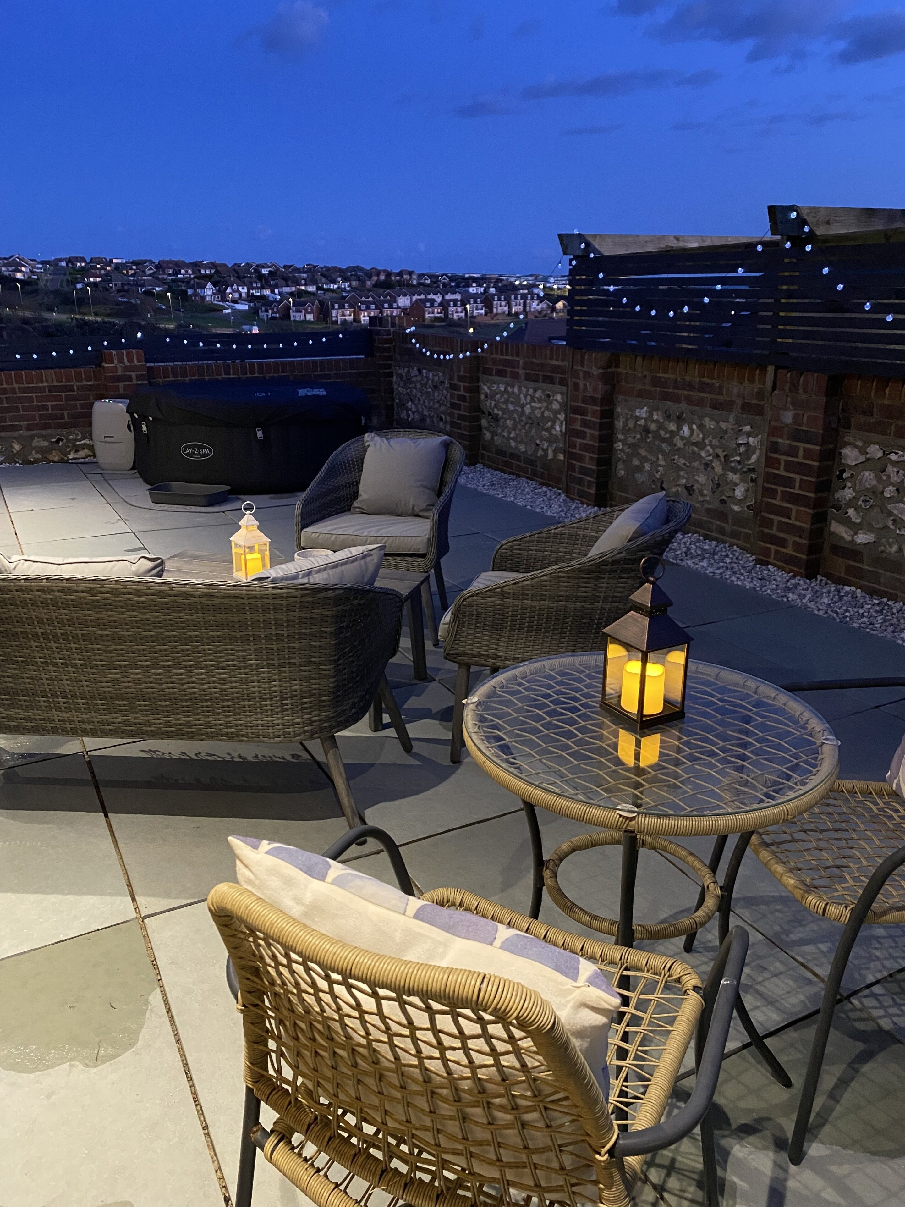 A rooftop patio with wicker furniture, a glass table, and a barbecue grill.