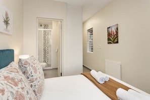 A hotel room with a bed, a bathroom with a shower, and a hallway with a radiator and artwork. - Sunset On Hill 3 (Cape Town)