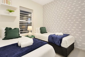 A hotel room with two beds, a window with blinds, a nightstand with a lamp, and a wall with a pattern of animal silhouettes.