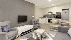 A modern living room with a flat-screen TV, grey sofas, a small table, and a kitchen area with white cabinets and appliances. - Sunset On Hill 3 (Cape Town)