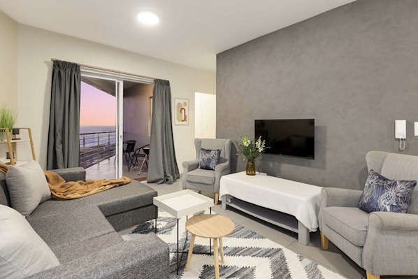A modern living room with a grey sofa, a coffee table, and a TV mounted on the wall.