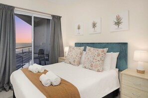 A hotel room with a bed, a nightstand, a lamp, and a view of the sea through a balcony. - Sunset On Hill 3 (Cape Town)