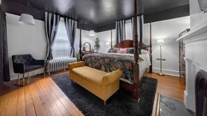 Un dormitorio con una cama con dosel, suelo de madera, radiador, sofá y chimenea.