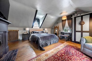 A bedroom with a sloped ceiling, a large bed, a desk with a chair, and a window with curtains.