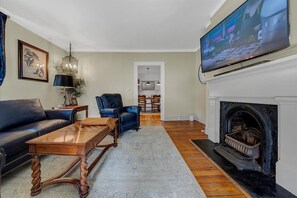 A living room with a fireplace, a television, a sofa, a coffee table, and a dining area in the background.