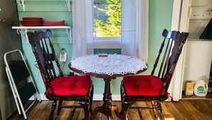 A dining area with a round table, two red cushioned chairs, a white doily, a telephone, and a shelf with red plates. - Bay Street Retreat - Waldport (Waldport)