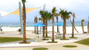 Une terrasse au bord de la plage, agrémentée de palmiers, de parasols bleus et d’une table blanche.