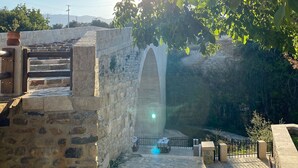 Un puente de piedra con un arco, rodeado de vegetación y un cielo despejado.