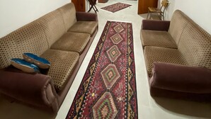 Amplia sala de estar con dos sofás color café estampados, un tapete rojo estampado y una lámpara de techo.