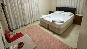 Un dormitorio con una cama, una mesa, una silla, una silla roja, una alfombra rosa y una lámpara en el techo.