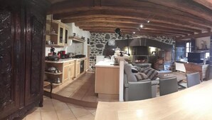 Une cuisine rustique aux murs en pierre, dotée d’un îlot central et d’un coin repas avec une table et des chaises en bois.