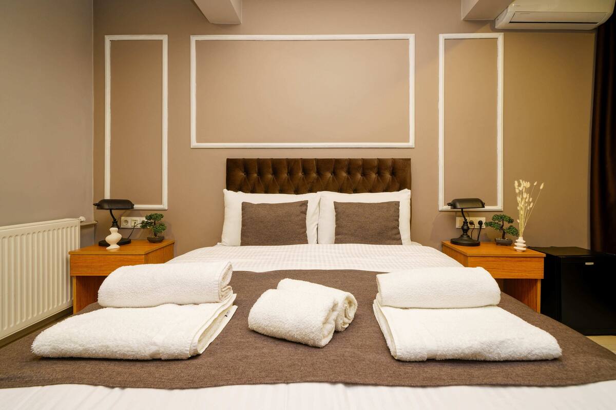 A hotel room with a large bed, two bedside tables, a headboard, and a radiator.
