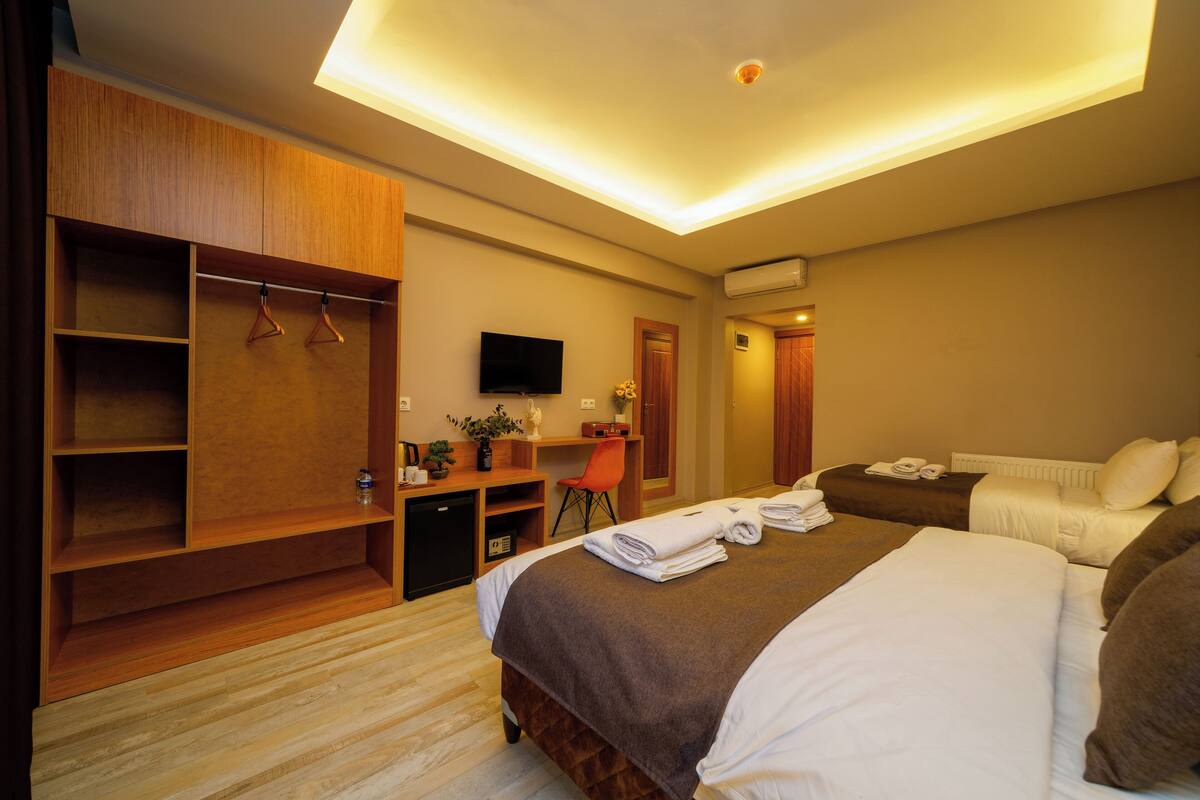 A hotel room with a large bed, a desk with a chair, a TV, and a wardrobe.