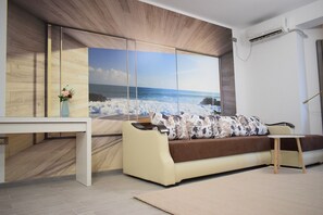 A modern living room with a large ocean view painting, a sofa, a small table, and a wooden floor.