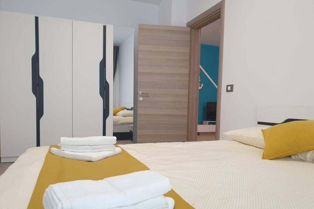 A hotel room with a bed, a yellow accent wall, a wardrobe, and a door leading to another room.