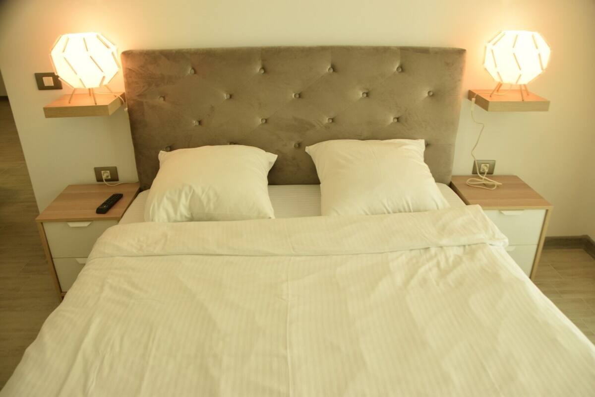 A bed with a tufted headboard, two bedside tables with lamps, and a remote control on one table.