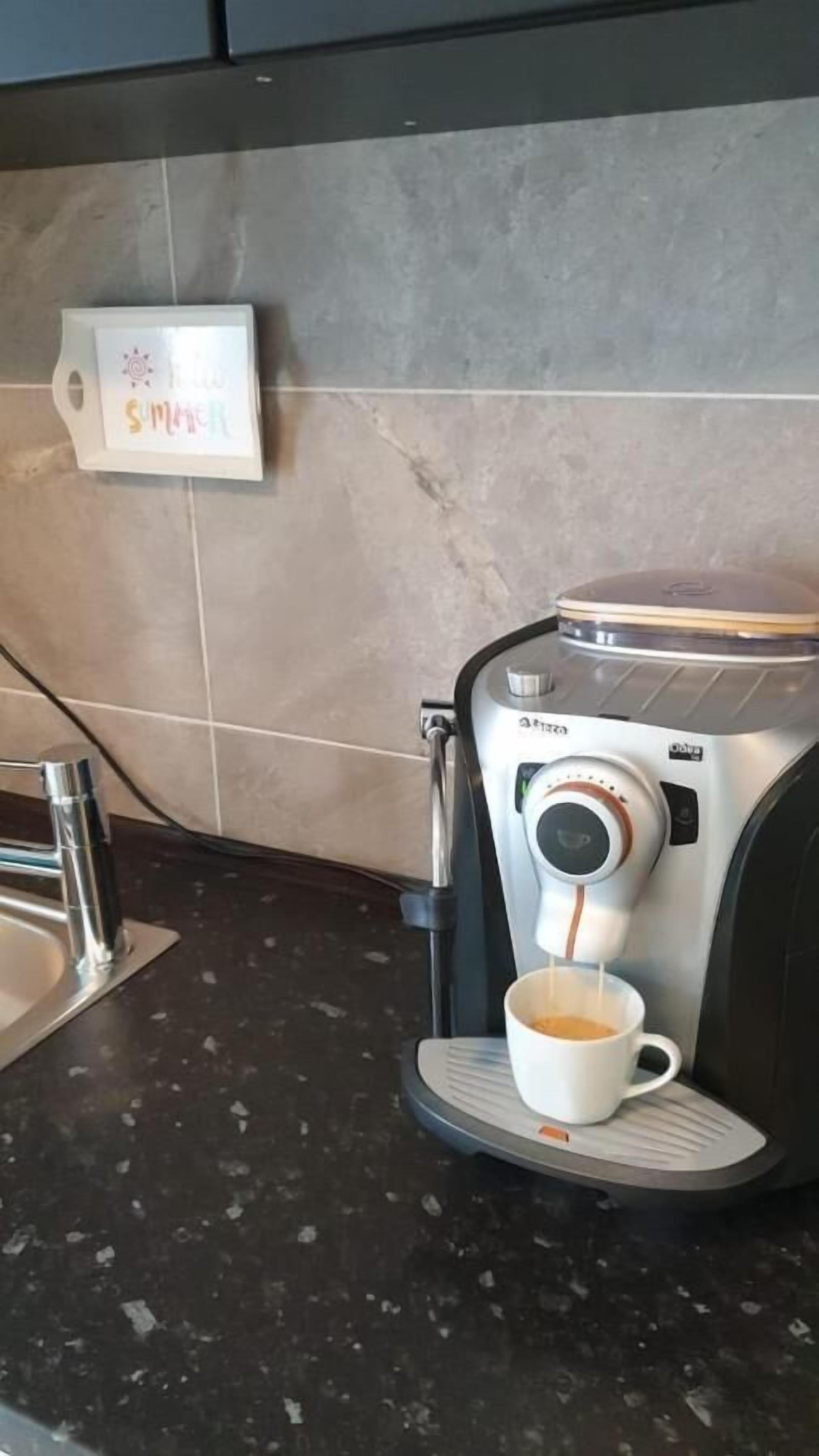 Una cocina con cafetera, un lavamanos y un cartel en la pared.