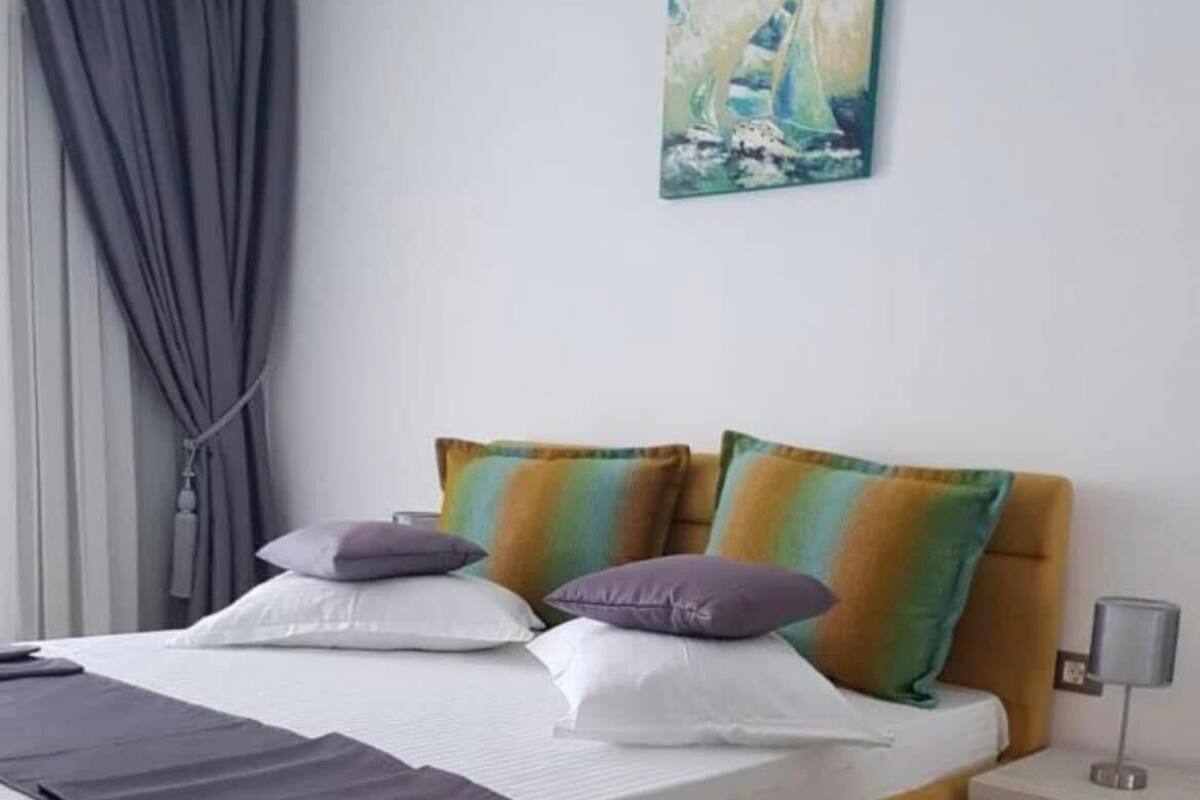 A bed with a headboard, a bedside table, a lamp, and a painting on the wall.