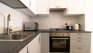 A compact kitchen with a stainless steel sink, a microwave, a stove, and a kettle.