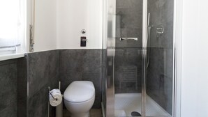 Moderni kylpyhuone, jossa on wc, lasinen suihkuseinä ja pyyhekoukku.