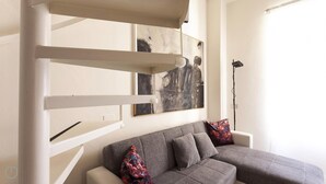 Uma sala de estar moderna com um sofá cinzento, duas almofadas decorativas e arte abstrata na parede.