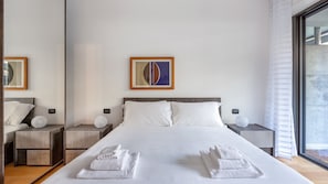 Una habitación de hotel moderna con una cama grande, dos mesitas de noche, un espejo y una obra de arte enmarcada en la pared.