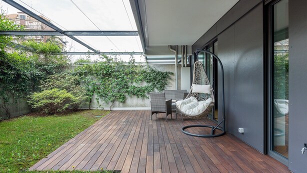 Eine moderne Terrassengestaltung mit Holzdeck, einer Hängematte und einer Glastür zu einem Gartenbereich mit viel Grün.