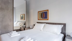 Ein modernes Hotelzimmer mit einem großen Bett, einem Nachttisch, einem Spiegel und einem gerahmten abstrakten Gemälde.
