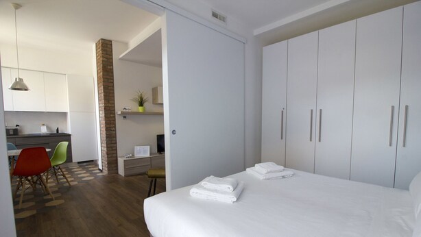 A hotel room with a bed, a desk with a computer, a chair, and a kitchenette. - Italianway Easy - Ciaia 6 A (Milan)