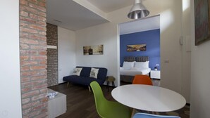 A modern room with a brick wall, a blue sofa with two pillows, a white round table, and a green chair. - Italianway Easy - Ciaia 6 A (Milan)