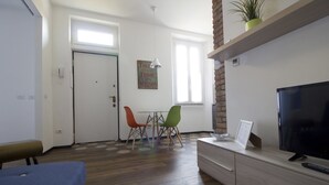 A modern living room with a television, a dining table with chairs, a bench, a plant on a shelf, and a door with a phone. - Italianway Easy - Ciaia 6 A (Milan)