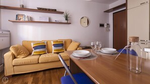 A modern living room with a sofa, a dining table set with plates and glasses, and a kitchen area with a microwave and a refrigerator. - Cirillo 14 - Apartment Milan (Milan)