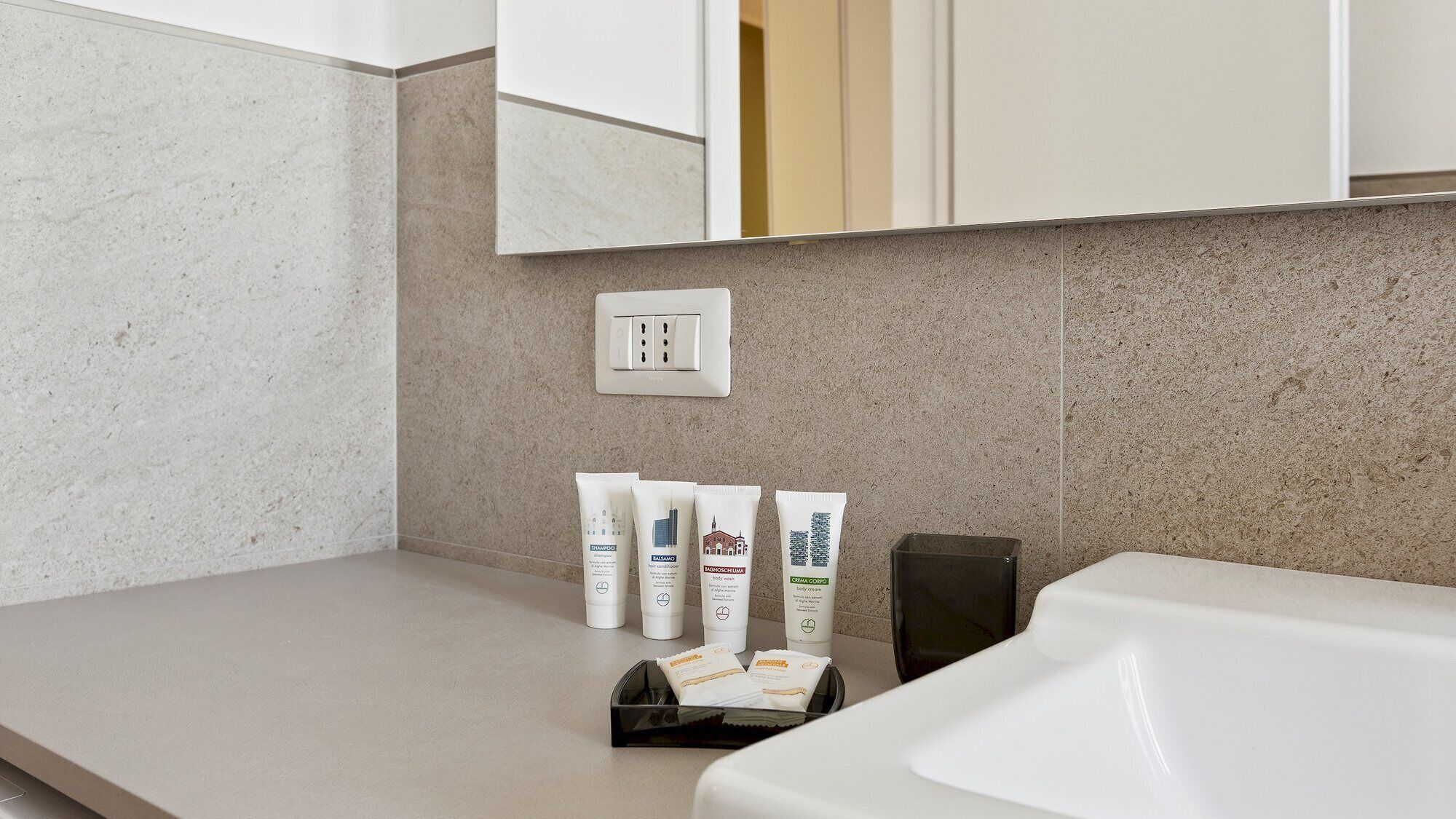 A bathroom with a beige countertop, a white sink, and toiletries including shampoo, body wash, and cream.