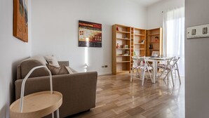 A living room with a sofa, a small wooden table, a dining table with chairs, a bookshelf, and a painting on the wall. - Italianway Easy - Argonne 7 (Milan)