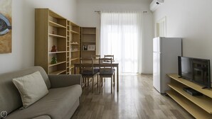 A living room with a sofa, a dining table with chairs, a TV on a stand, and a large wooden bookshelf. - Italianway Easy - Argonne 7 (Milan)