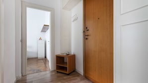 A hallway with a wooden door, a white wall with a coat hook, and a small wooden shelf with a magazine. - Italianway Easy - Argonne 7 (Milan)