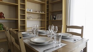 A dining table set with plates, glasses, and cutlery, surrounded by wooden chairs and shelves with kitchenware. - Italianway Easy - Argonne 7 (Milan)
