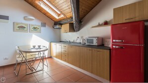 A kitchen with wooden cabinets, a red refrigerator, a microwave, and a dining table with chairs.
