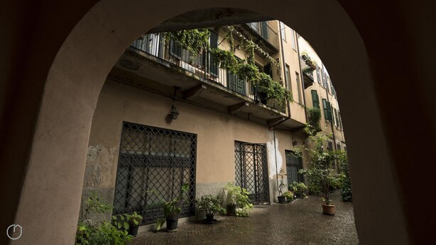 An arched corridor with a cobblestone path, potted plants, and a building with barred windows and balconies. - Italianway Easy - Argelati 12 Bilo (Milan)