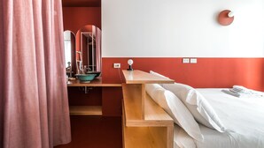 Hotelkamer met een houten bureau, een wastafel met een turquoise kom, een bed met witte lakens en een rode accentmuur.