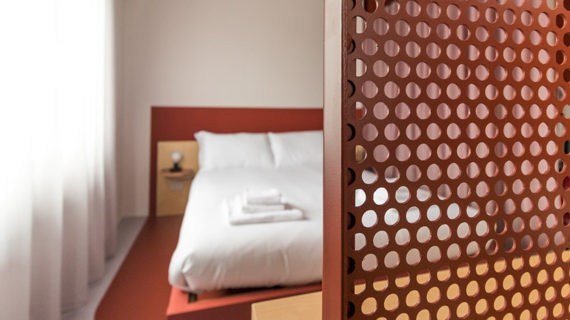 A neatly made bed with white linens and a red headboard in a hotel room.
