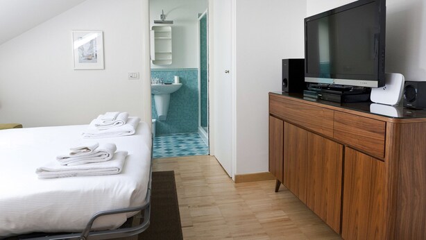 Hotellihuone, jossa on sänky, televisio ja puinen kaappi.