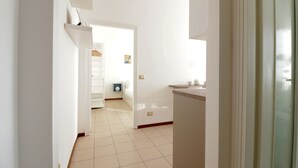 A hallway with a white door, a small seating area with a blue chair, and a white shelf with a white object on it. - Italianway Comfort - Bergognone 47 B (Milan)