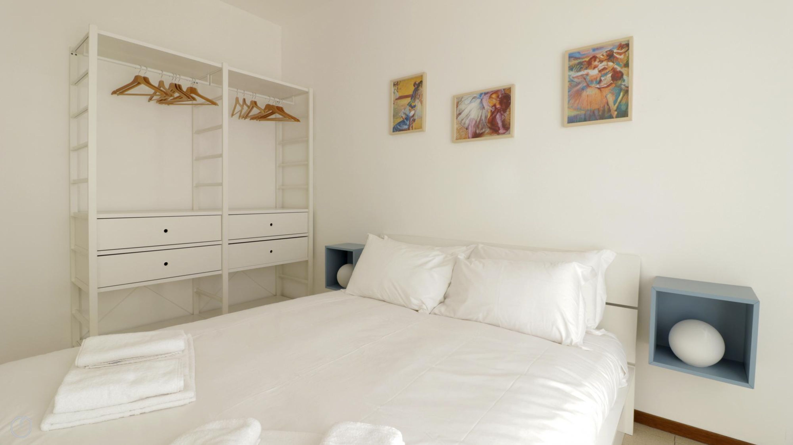 Un dormitorio con una cama, un armario y tres cuadros en la pared.