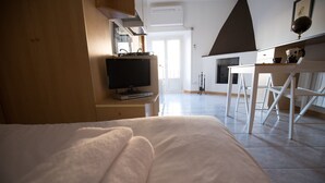 Et soveværelse med seng, fjernsyn på et stativ, et skrivebord med stol og udsigt ud.
